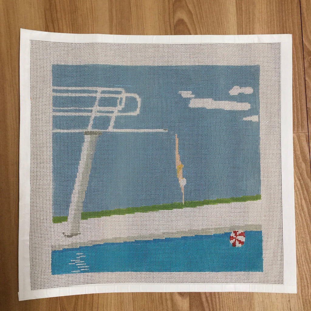 needlepoint pool scene with diving board and pool ladder on a wooden surface