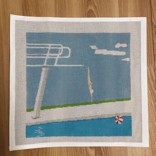 needlepoint pool scene with diving board and pool ladder on a wooden surface