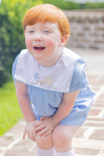 Child with red hair wearing a blue dress with a white collar outdoors.