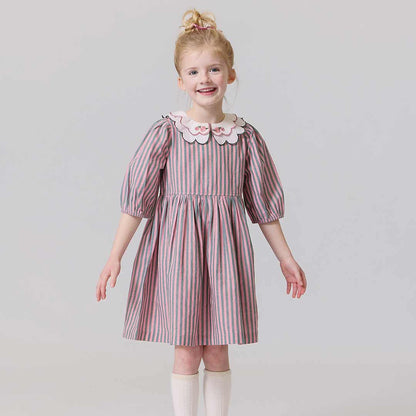 Young girl wearing a striped dress with a white collar against a plain background