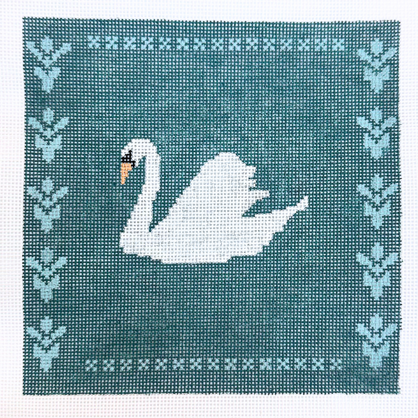 A square needlepoint canvas featuring a white swan with a yellow beak on a teal background, framed by a border of light blue floral motifs and white geometric patterns.