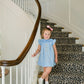 Young girl in a blue dress standing on a leopard print staircase.