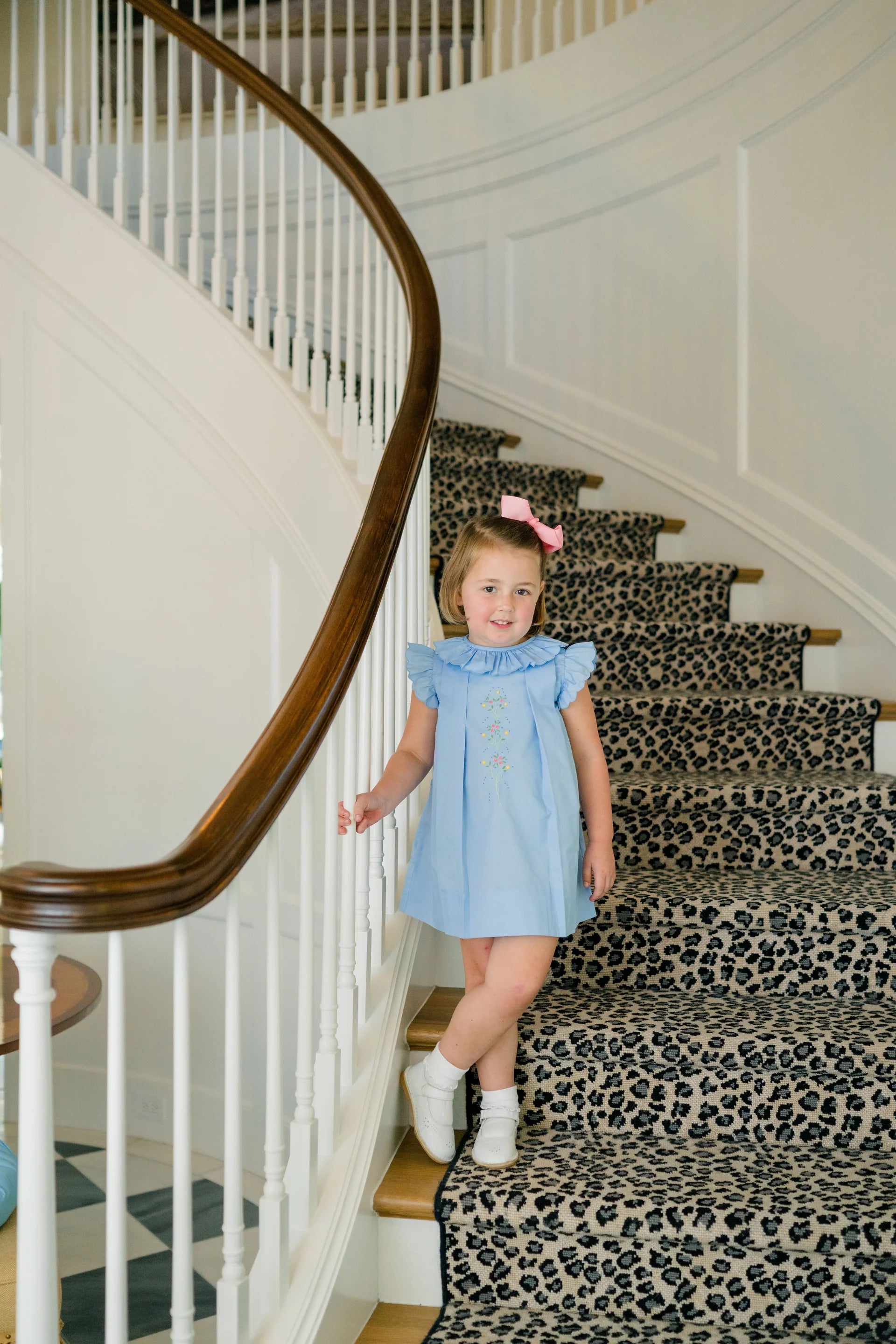 Young girl in a blue dress standing on a leopard print staircase.