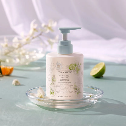 Thymes bergamot and neroli lotion bottle on a clear dish with flowers and fruits in the background