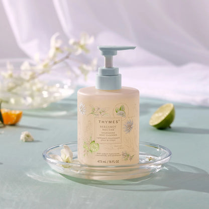 Thymes body wash bottle on a glass dish with flowers and fruit in the background