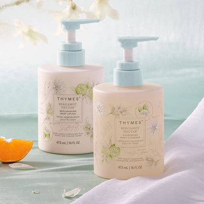 Two Thymes body care products on a light blue background with an orange slice and flowers.