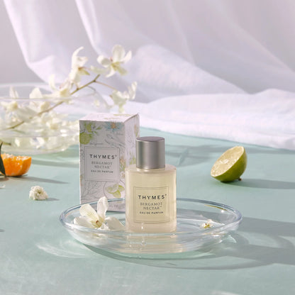 Thymes Bergamot Nectar perfume bottle and packaging on a light green surface with flowers and fruits.