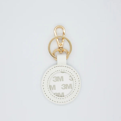 A white circular keychain or bag charm with a gold-tone metal clasp and key ring, featuring a white strap and a printed white-on-white circular insert with repeating '3M' branding.