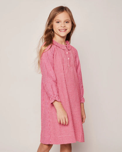 Young girl wearing a red checkered dress against a plain background