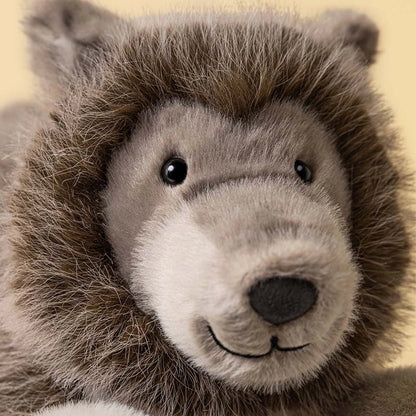 Close-up of a plush stuffed animal head with brown and gray fur, black eyes, and a stitched smile on a pale yellow background.