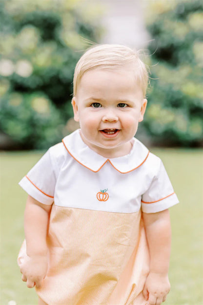 Child wearing a white shirt with an orange pumpkin design outdoors