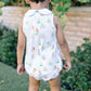 Child wearing a sleeveless romper with sailboat pattern and yellow rain boots outdoors.