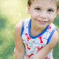 Young boy in a sleeveless shirt with red lettering sitting on grass