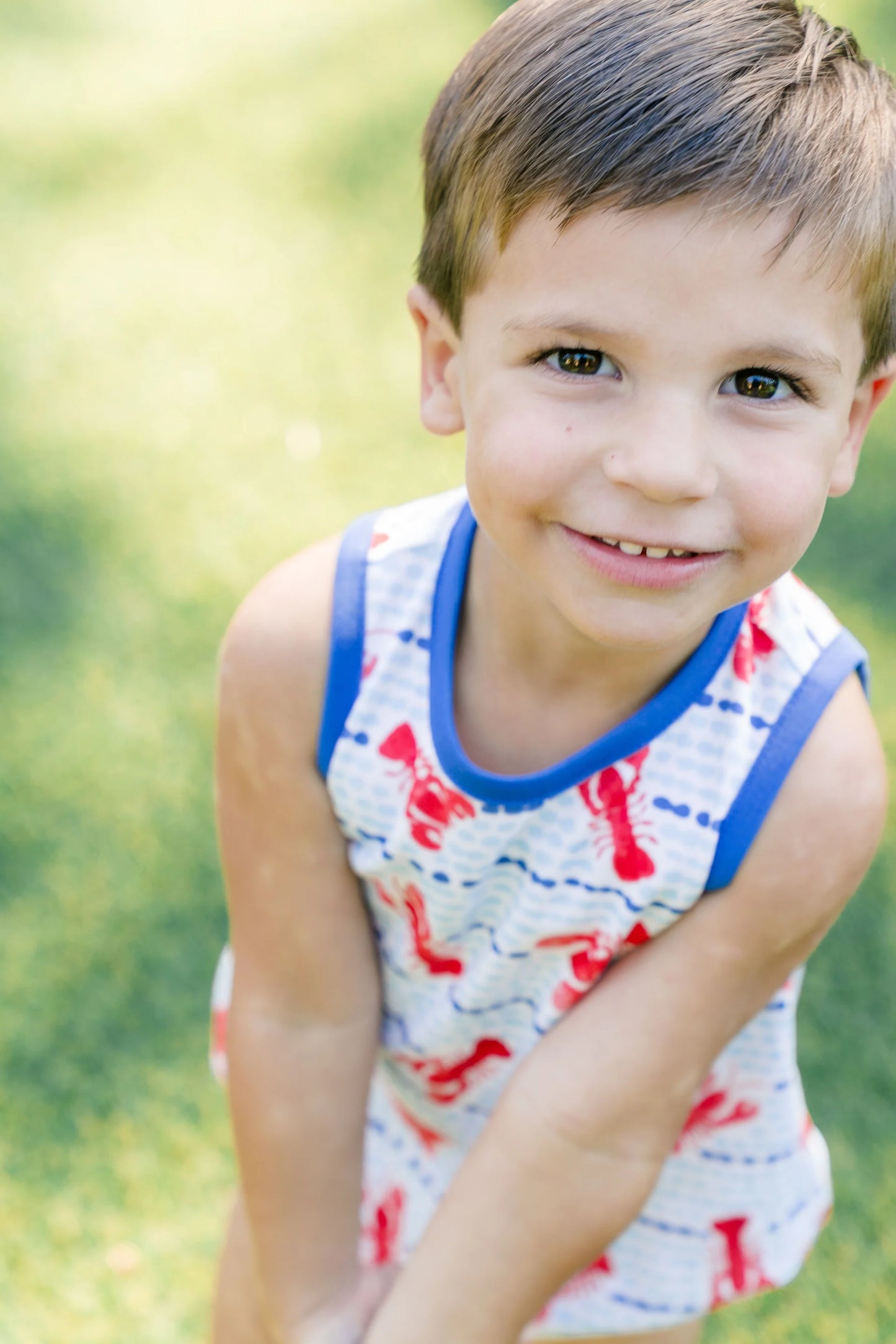 Young boy in a sleeveless shirt with red lettering sitting on grass