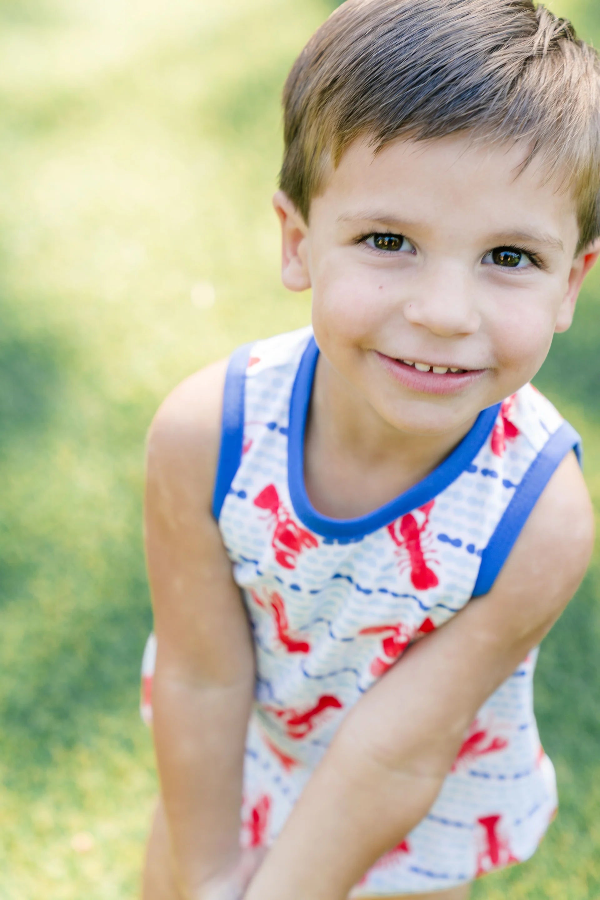 Young boy in a sleeveless shirt with red lettering sitting on grass
