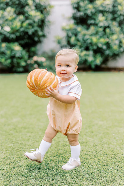 Child holding a pumpkin on grass with blurred greenery