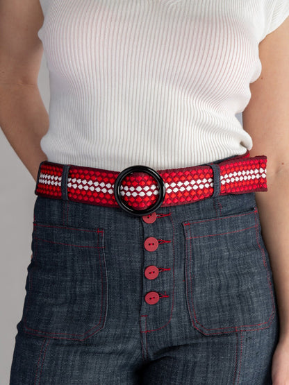 Person wearing a red and white beaded belt with a black buckle on dark jeans.