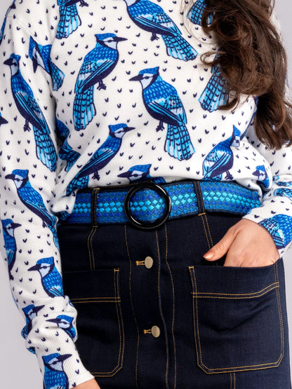 Person wearing a white shirt with blue bird pattern and dark jeans with a blue belt.