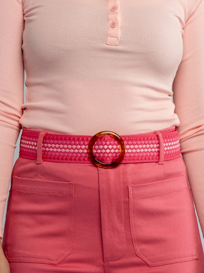 Person wearing a pink skirt with a red belt and gold buckle against a light pink background