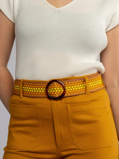 Person wearing a white top and mustard yellow pants with a woven belt.