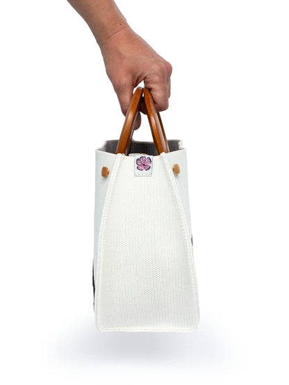 Hand holding a white tote bag with wooden handles on a white background