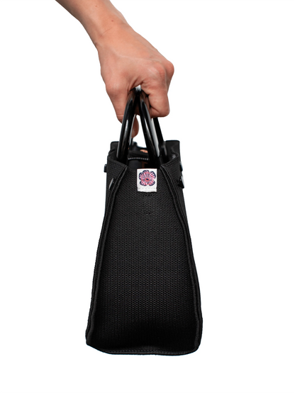 Black bag held by a hand with a visible brand logo on a white background