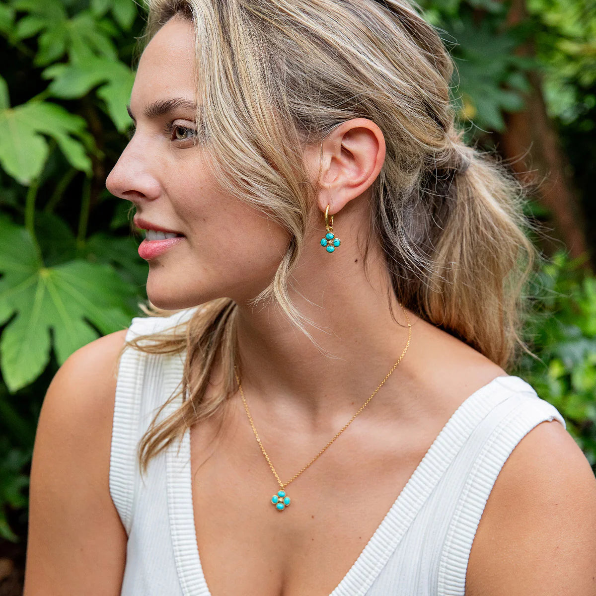 Woman wearing turquoise earrings and a necklace with a green leafy background