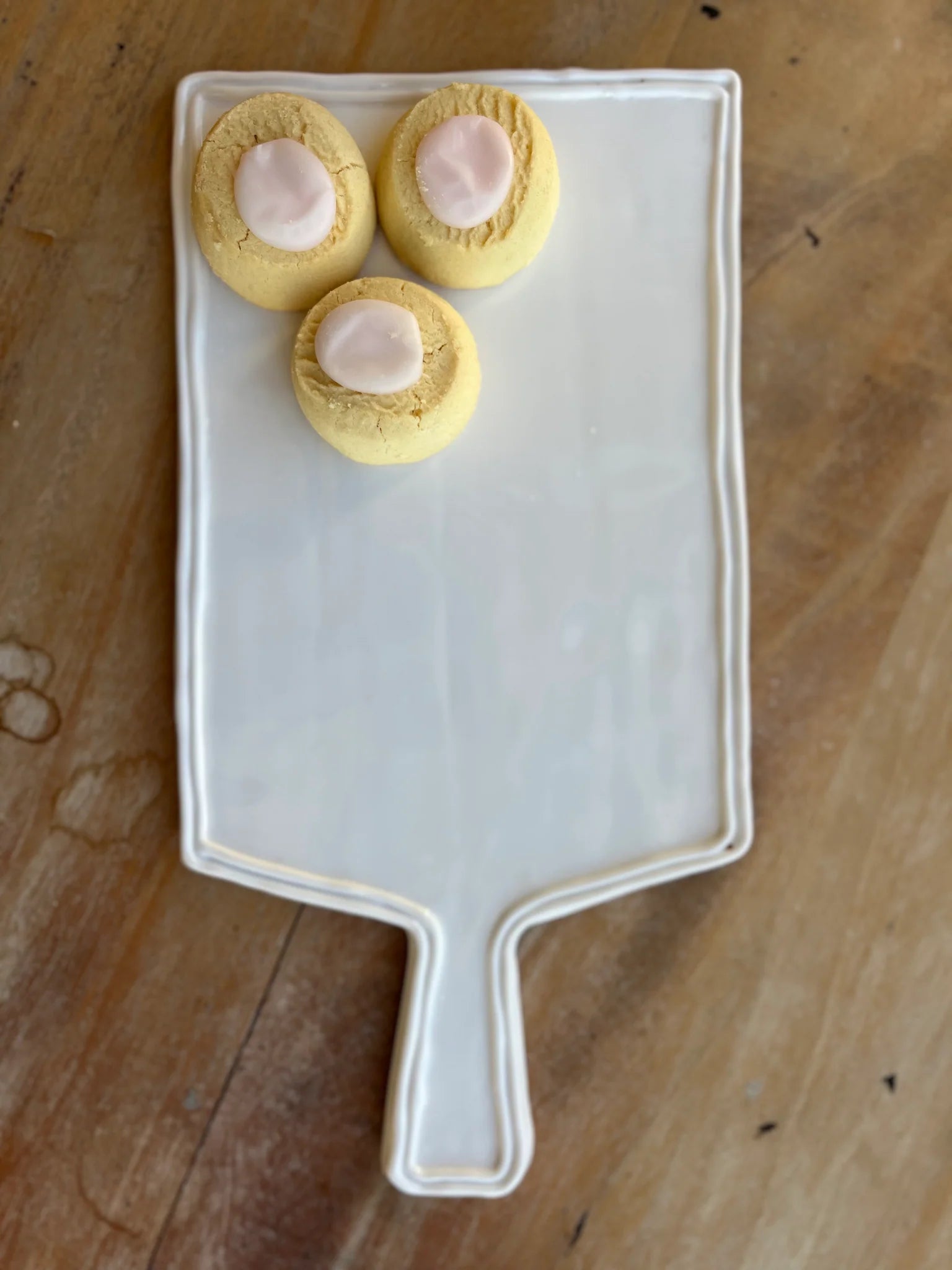 Three small round pastries with a pink center on a white rectangular plate with a handle, placed on a wooden surface.