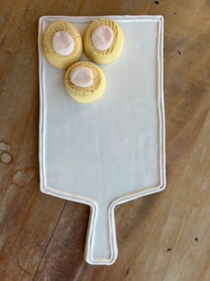 Three small round pastries with a pink center on a white rectangular plate with a handle, placed on a wooden surface.