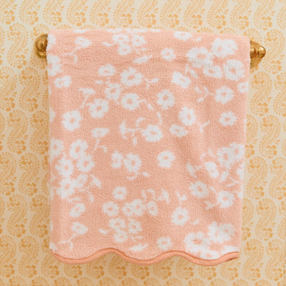 Pink floral towel hanging on a gold towel rack against a beige wallpapered wall.