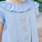 Light blue dress with floral embroidery worn by a child, against a blurred green background