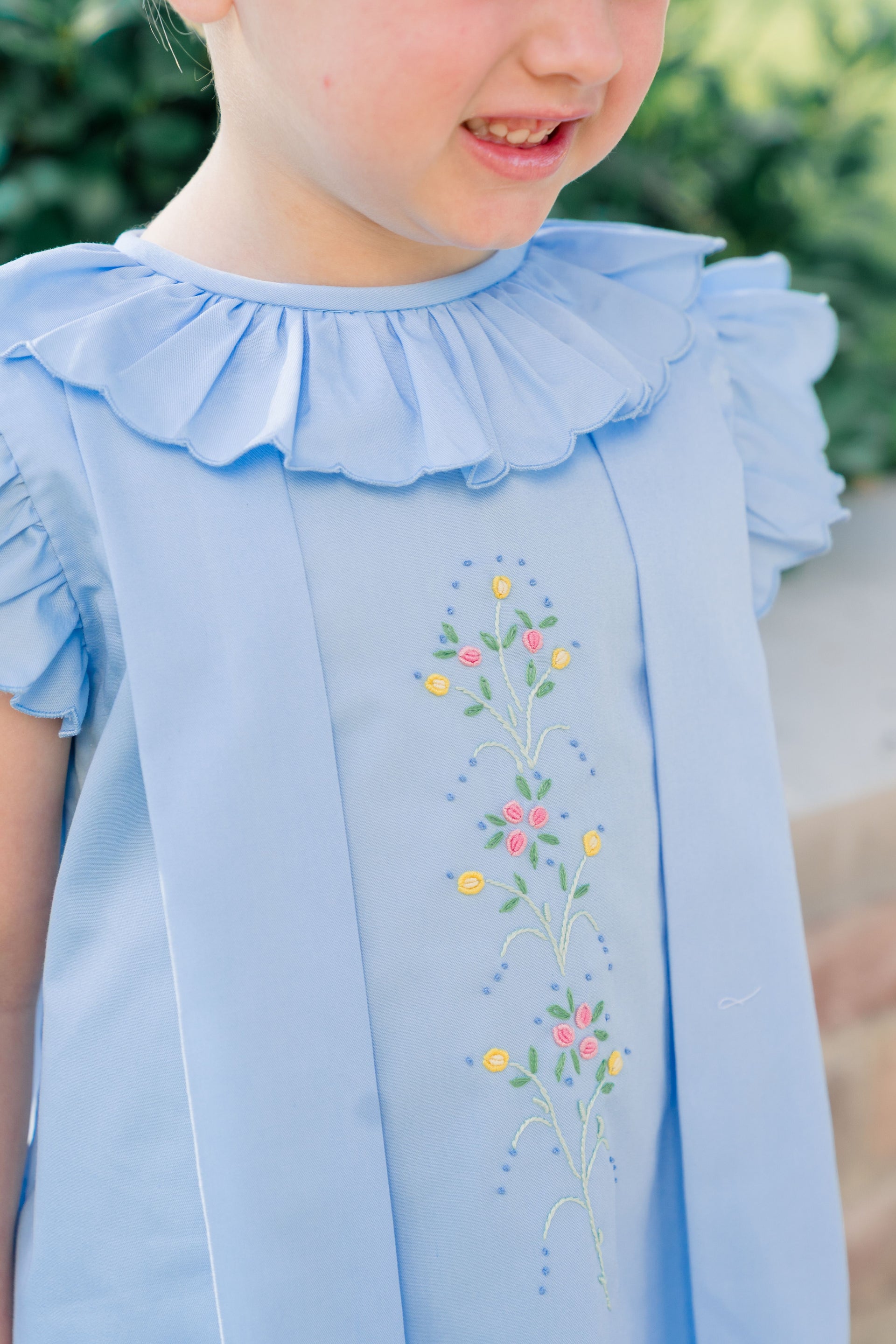 Light blue dress with floral embroidery worn by a child, against a blurred green background
