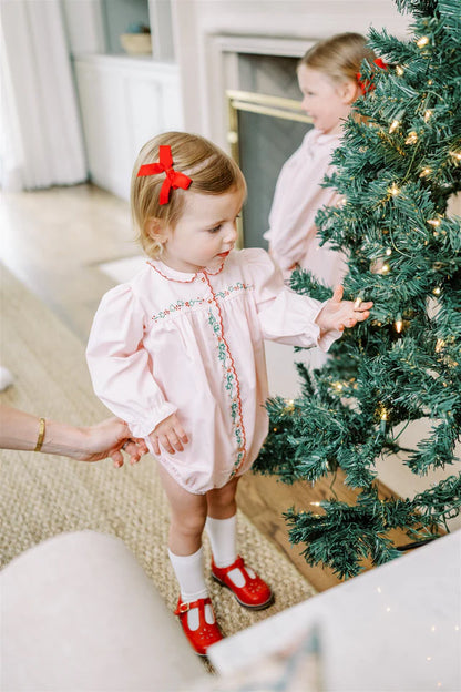 Two young girls in pink dresses standing near a decorated Christmas tree.