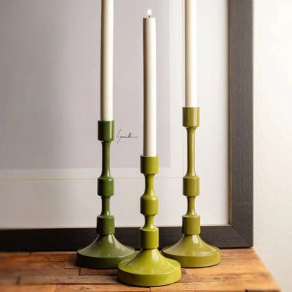 Three green candle holders with white candles on a wooden surface.