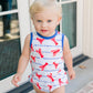 Child wearing a red and blue swimsuit with lobster pattern standing in front of a glass door.