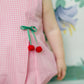 Child wearing a pink checkered romper with cherry details against a floral background