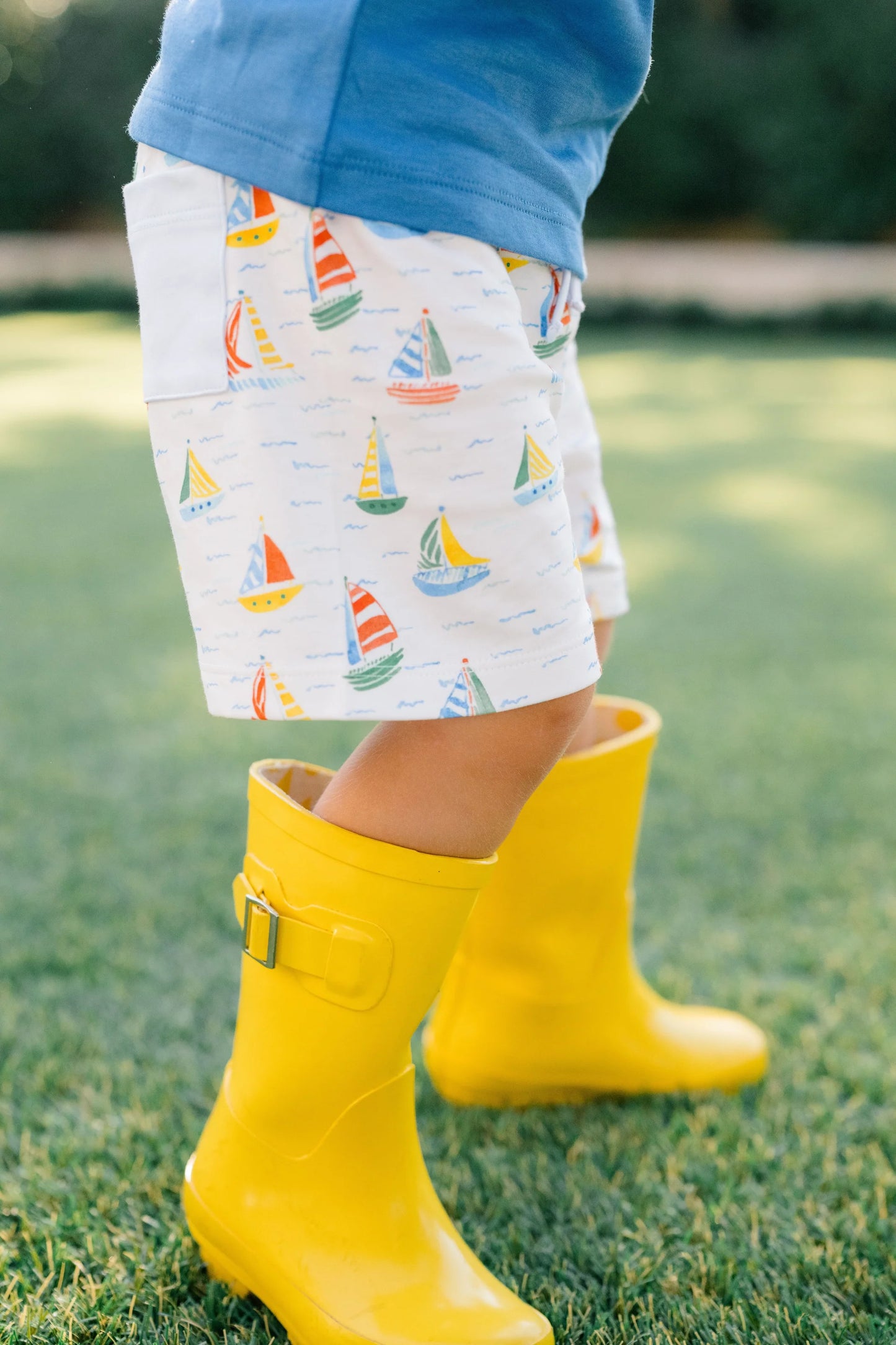 Child wearing yellow rain boots and patterned shorts on grass