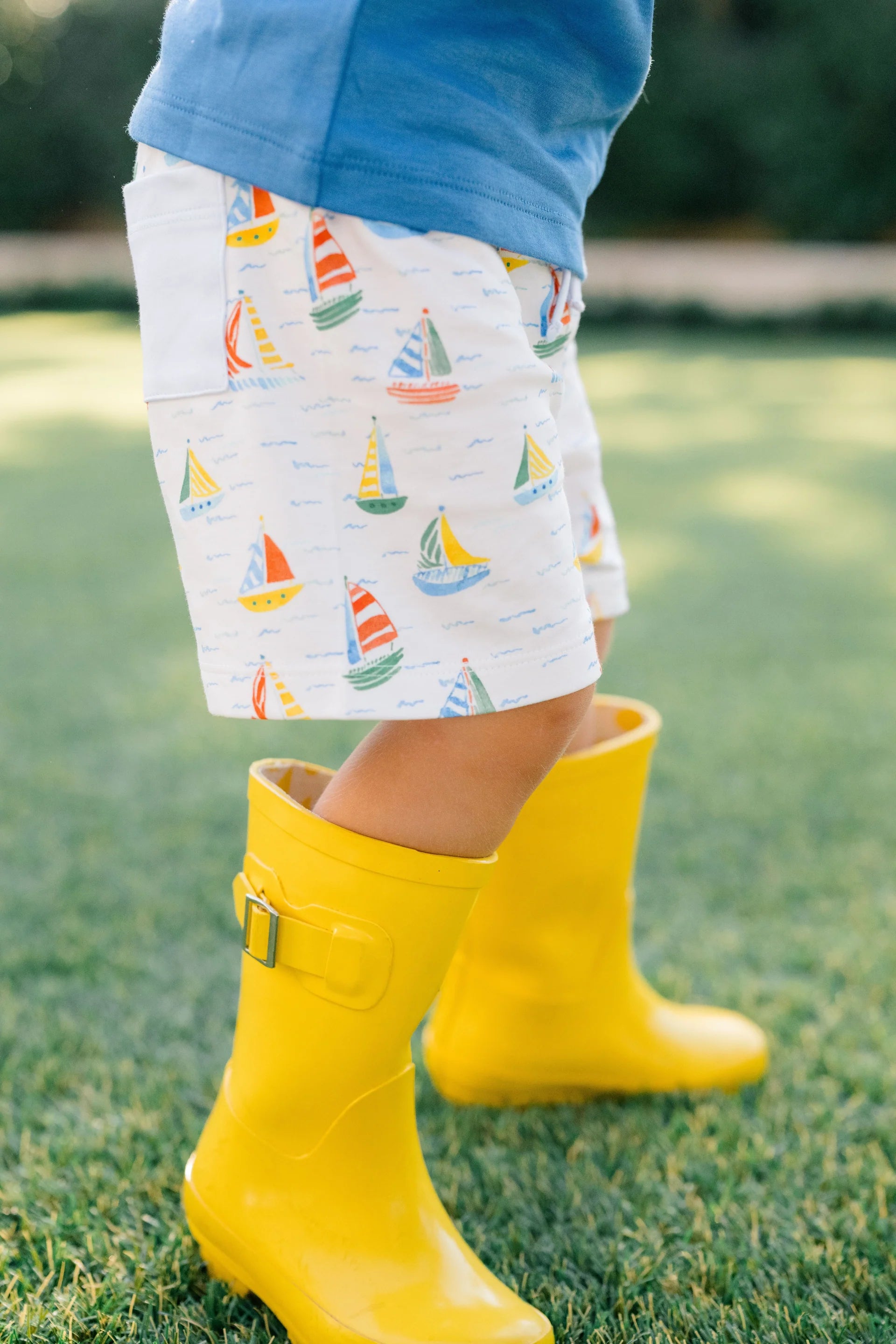 Child wearing yellow rain boots and patterned shorts on grass