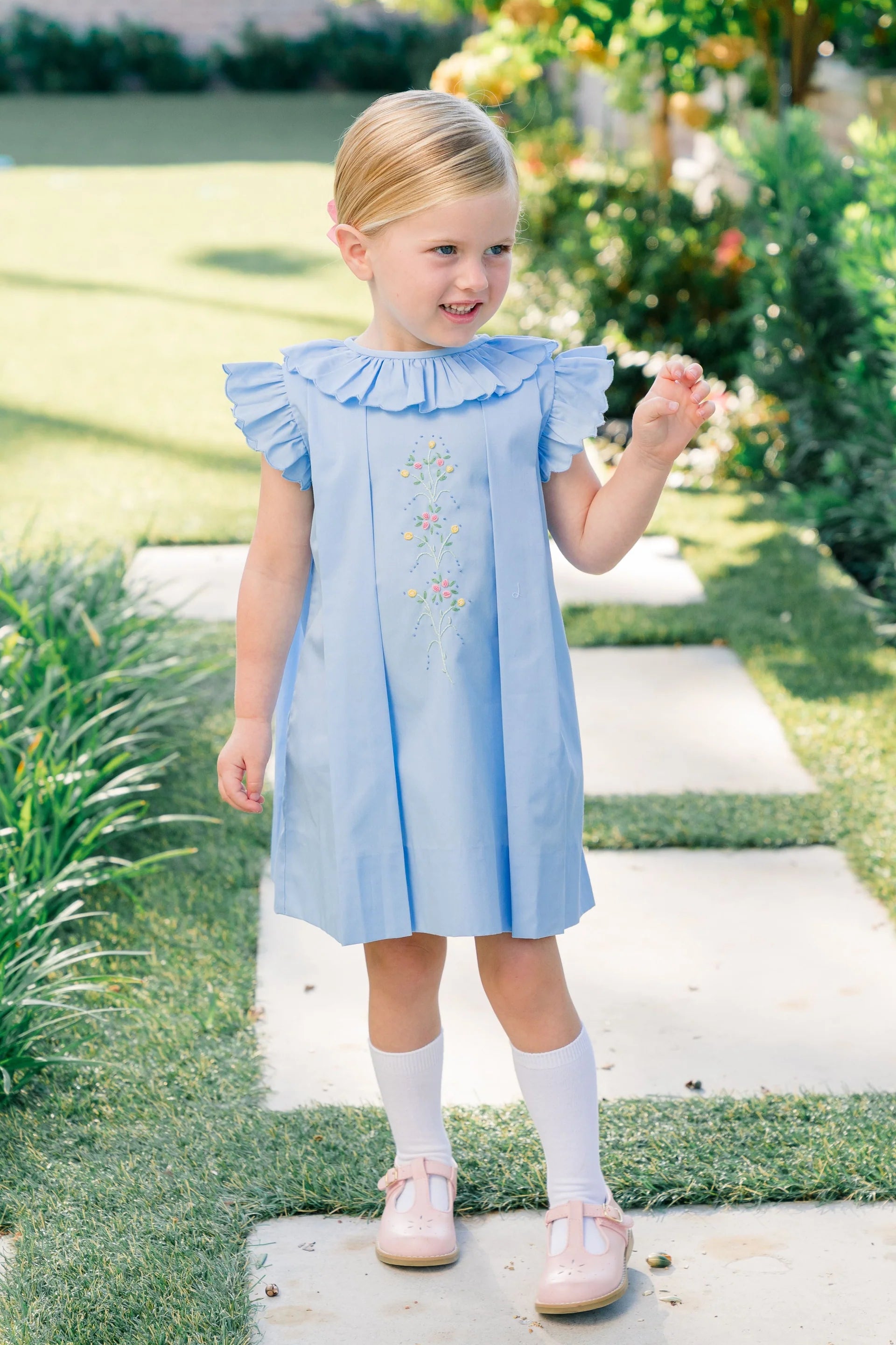 Young girl in a blue dress standing on a garden path.