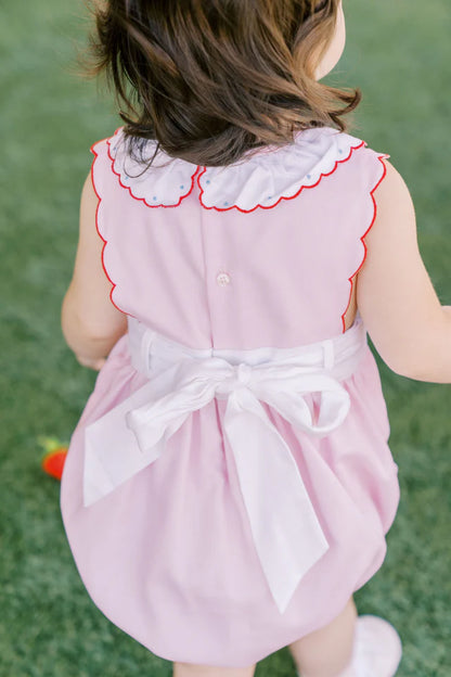 A pink baby bubble romper with white trim and strawberry appliques on the pockets and a ruffled collar.