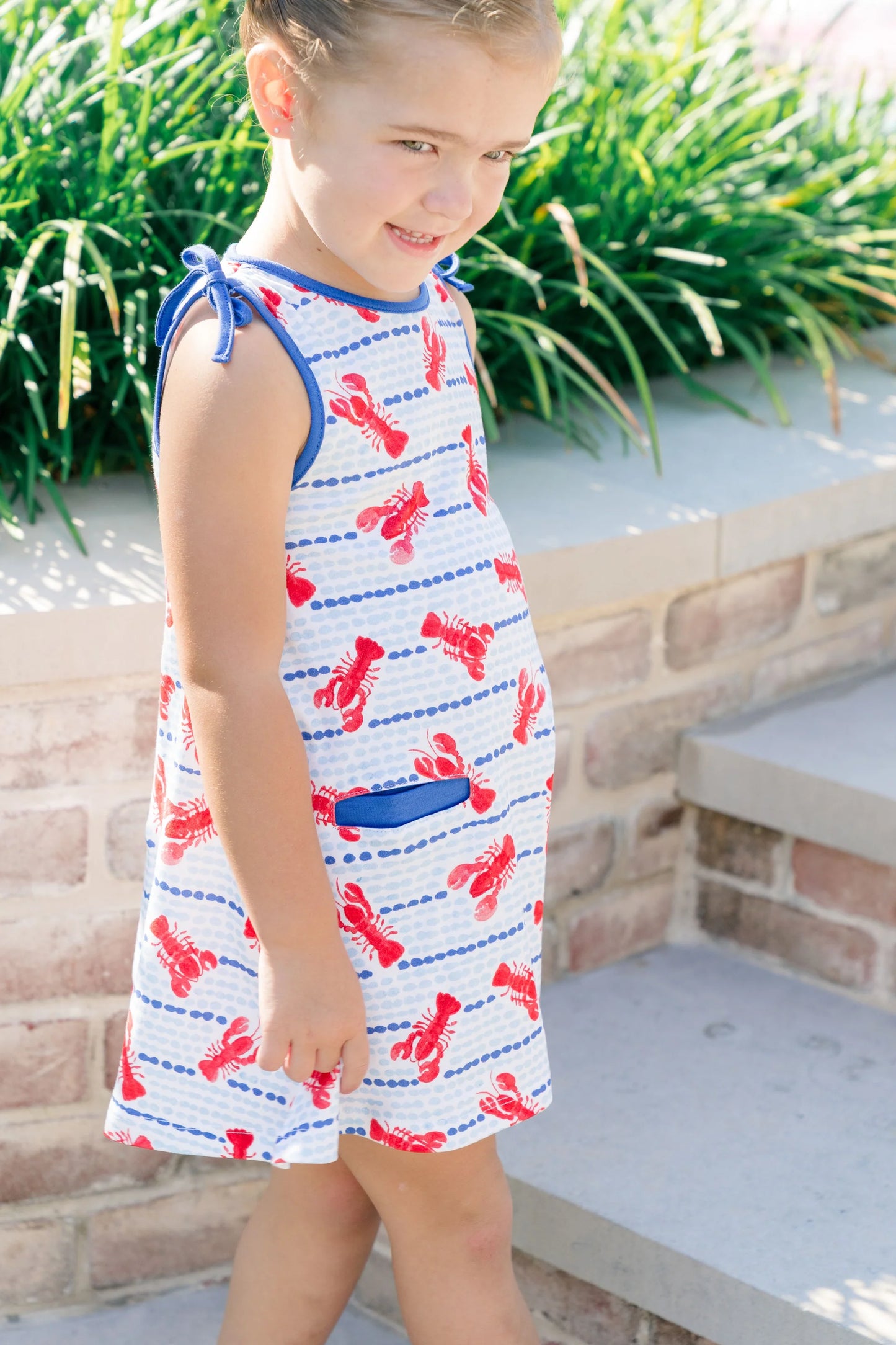 Young girl wearing a dress with red lobster pattern outdoors.