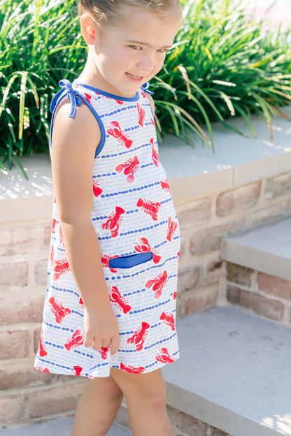 Young girl wearing a dress with red lobster pattern outdoors.