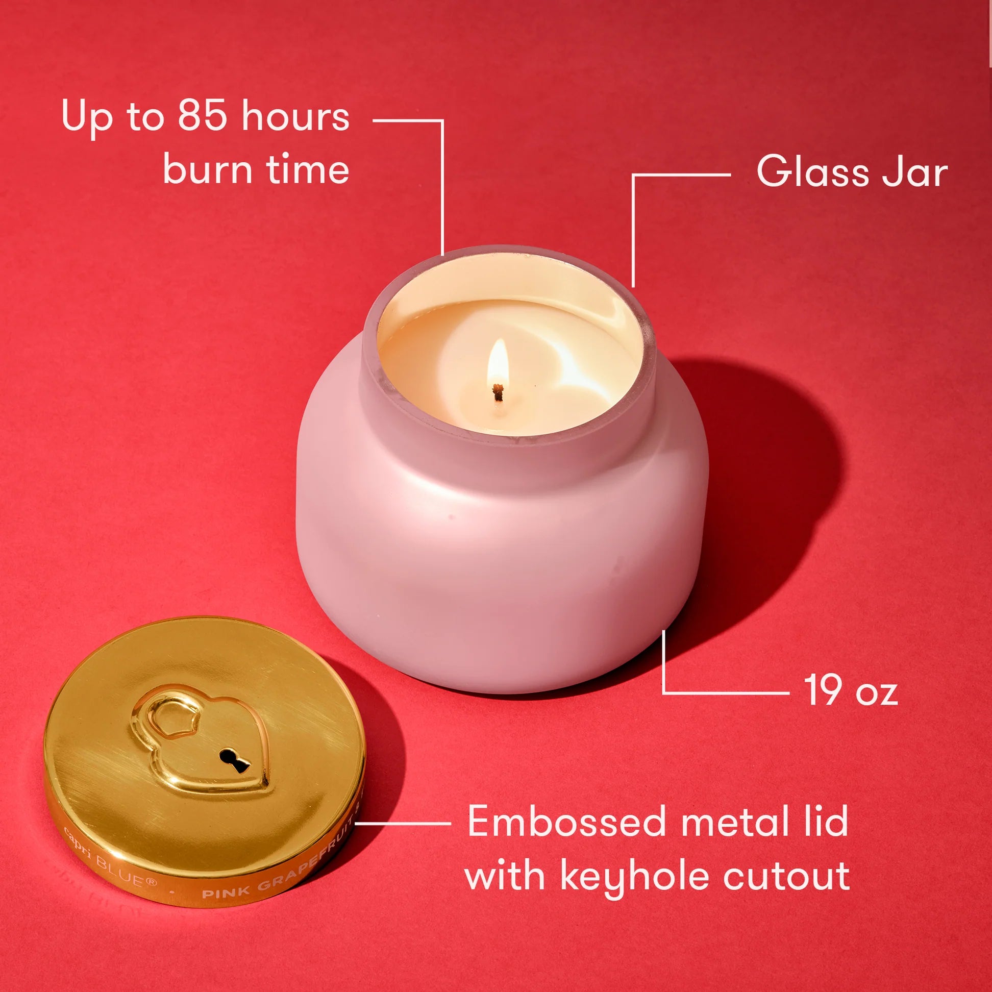 Pink candle in a glass jar with gold lid on a red background, showing features like burn time and weight.