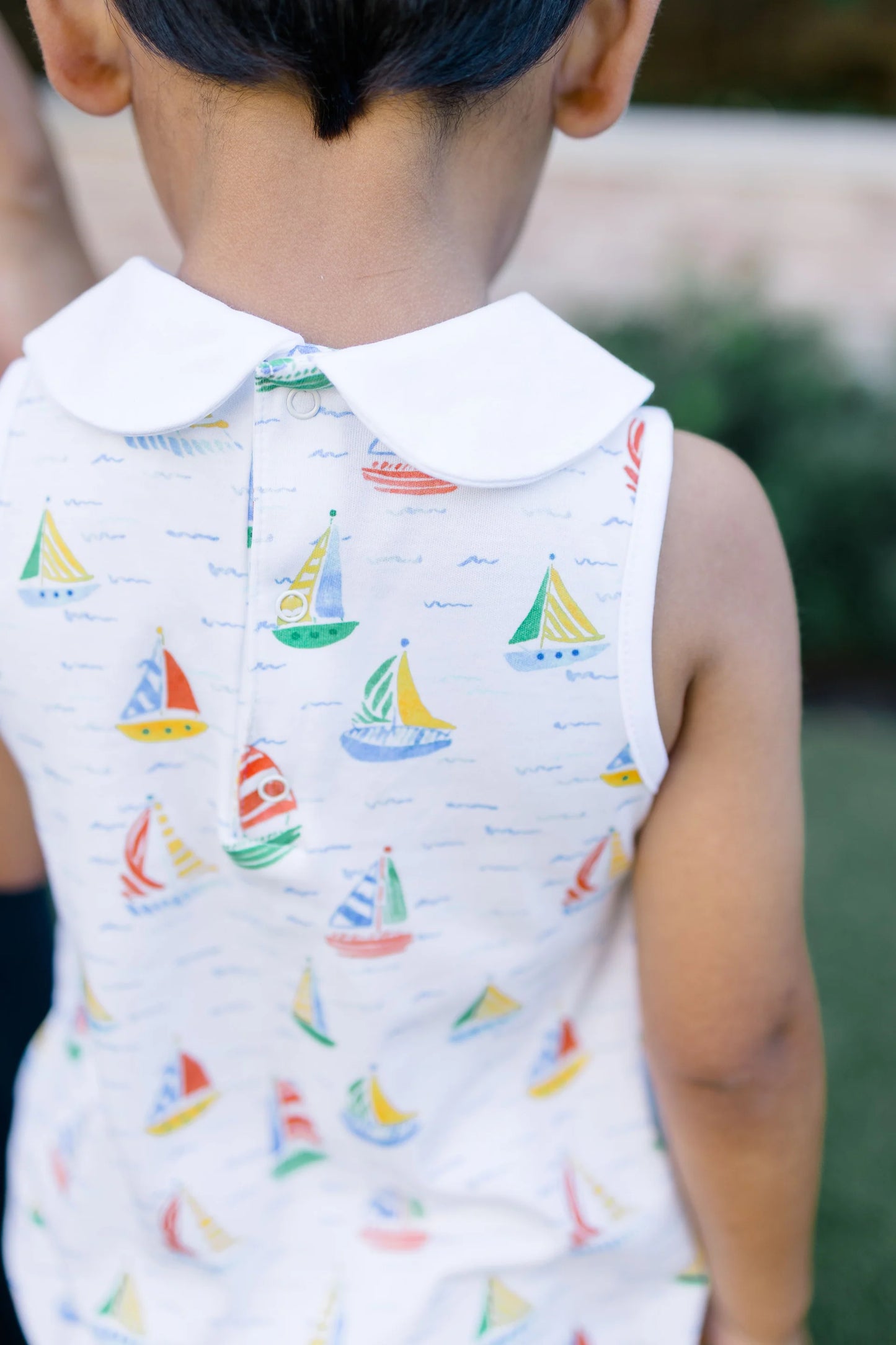 Child wearing a sleeveless shirt with sailboat pattern outdoors