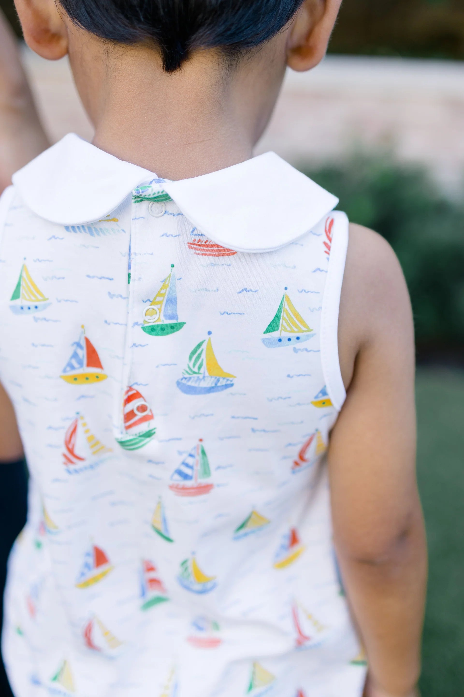 Child wearing a sleeveless shirt with sailboat pattern outdoors