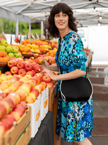 Woman in a colorful dress at an outdoor market with fruits and vegetables.