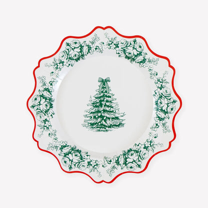 A white paper plate with a scalloped edge, featuring a green Christmas tree motif in the center and a border of green floral toile pattern, finished with a red scalloped rim.