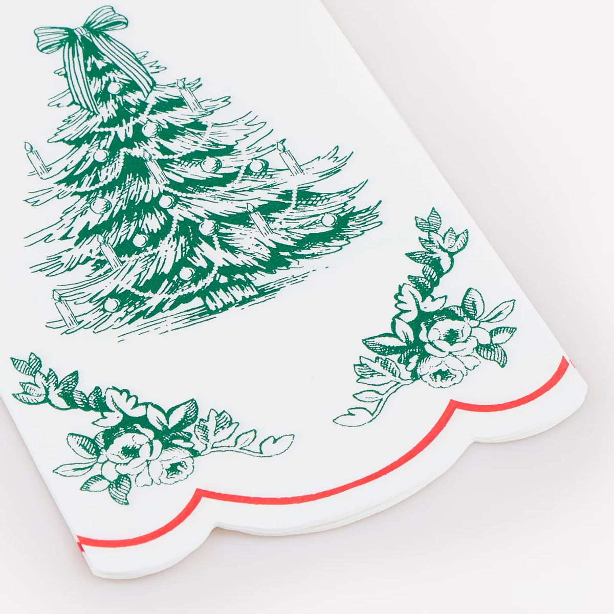 A white kitchen towel with a green Christmas tree and floral pattern, finished with a scalloped edge and a thin red line.