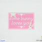 Cross-stitched pattern with 'some bunny loves you' text on a pink background