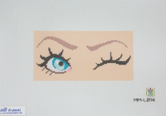 Cross-stitched design of an eye with eyelashes on a beige background, featuring the brand 'Milli Tomas' logo.